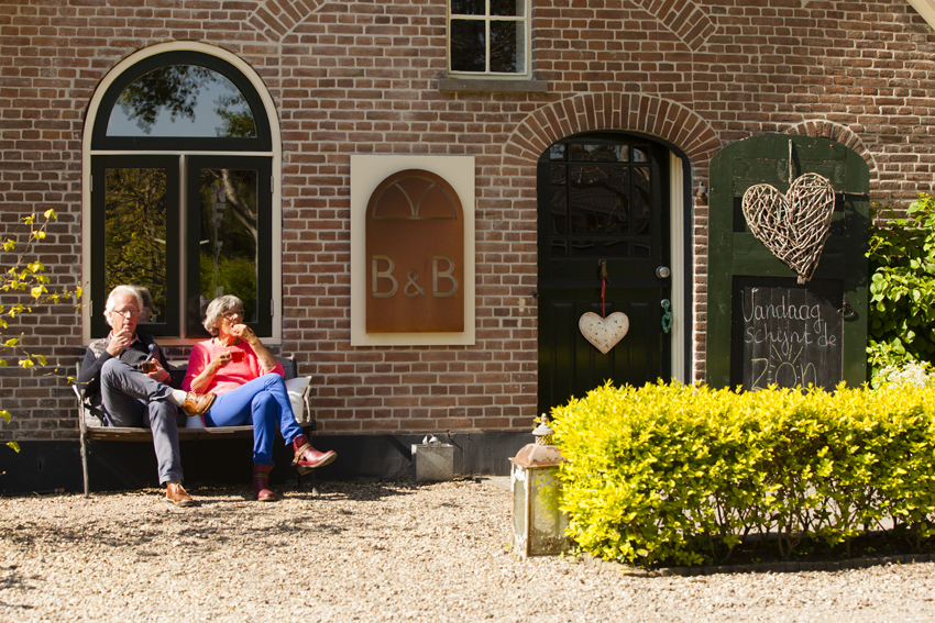 Gasten op het bankje voor de gevel van het bakhuis met de groene deuren
